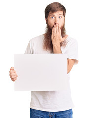 Poster - Handsome young red head man with long beard holding blank empty banner covering mouth with hand, shocked and afraid for mistake. surprised expression