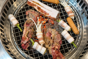 Wall Mural - Raw beef and bacon roll with enoki mushroom and vegetable on yakiniku stove which has hot charcoal. Barbecue Japanese style. Yakiniku. Is the Japanese version of Korean BBQ. Barbecue grilled on stove.