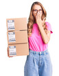 © Krakenimages.com - Young caucasian woman with blond hair holding delivery package covering mouth with hand, shocked and afraid for mistake. surprised expression