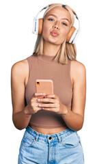 Canvas Print - Beautiful young blonde woman using smartphone wearing headphones looking at the camera blowing a kiss being lovely and sexy. love expression.