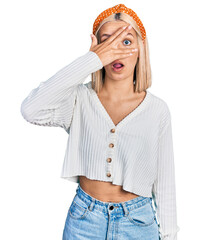 Sticker - Beautiful young blonde woman wearing casual white sweater peeking in shock covering face and eyes with hand, looking through fingers with embarrassed expression.