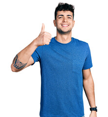 Wall Mural - Young hispanic man wearing casual t shirt doing happy thumbs up gesture with hand. approving expression looking at the camera showing success.