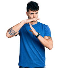 Wall Mural - Young hispanic man wearing casual t shirt doing time out gesture with hands, frustrated and serious face