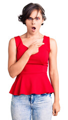 Sticker - Beautiful young woman with short hair wearing casual style with sleeveless shirt surprised pointing with finger to the side, open mouth amazed expression.