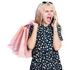 Canvas Print - Young caucasian woman holding shopping bags and talking on the smartphone angry and mad screaming frustrated and furious, shouting with anger. rage and aggressive concept.