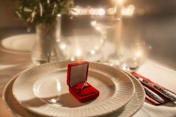 holidays, valentine's day and proposal concept - close up of engagement ring in red box on served table at home