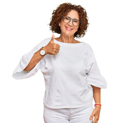 Wall Mural - Beautiful middle age mature woman wearing casual clothes and glasses doing happy thumbs up gesture with hand. approving expression looking at the camera showing success.