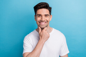 Wall Mural - Photo of cheerful positive guy wear white t-shirt smiling hand arm chin isolated blue color background