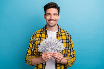 Sticker - Portrait of successful positive guy with stubble wear checkered shirt hold bunch of dollars in arms isolated on blue color background