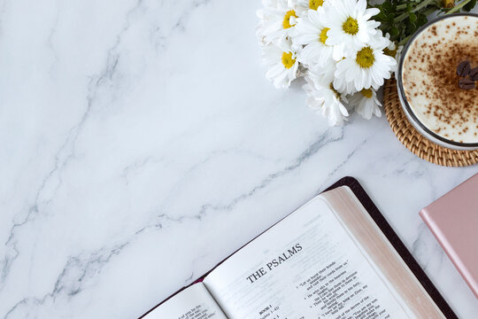Psalms open holy bible book on white marble background with coffee cup and flowers. Top table view. Copy space. Studying Old Testament Christian Scriptures.