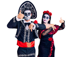 Poster - Young couple wearing mexican day of the dead costume over background doing thumbs up and down, disagreement and agreement expression. crazy conflict