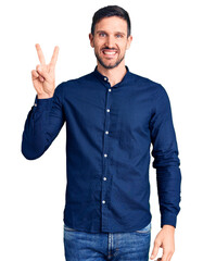 Wall Mural - Young handsome man wearing casual shirt smiling looking to the camera showing fingers doing victory sign. number two.