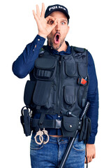 Canvas Print - Young handsome man wearing police uniform doing ok gesture shocked with surprised face, eye looking through fingers. unbelieving expression.