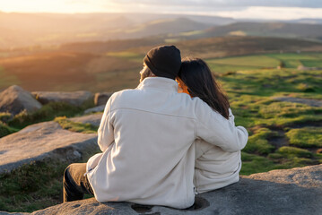 Back view of the happy couple in love sitting on top of a mountain enjoying a sunset landscape view  success life concept breath passion wisdom wellbeing