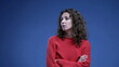 © Marco - Woman feeling bored sighing deeply with arms crossed looking up and rolling eyes in boredom standing on blue backdrop