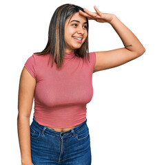 Poster - Young hispanic girl wearing casual t shirt very happy and smiling looking far away with hand over head. searching concept.