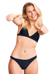 Poster - Young beautiful blonde woman wearing bikini approving doing positive gesture with hand, thumbs up smiling and happy for success. winner gesture.