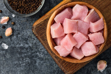 Diced raw chicken breast in wooden bowl on black background.