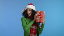 Smiling Attractive Young Woman With Dark Short Hair With Red Checkered Scarf Holding Box Wrapped In Checkered Paper, Shaking Xmas Gift, Posing For Camera. High Quality 4k Footage