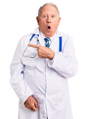 Canvas Print - Senior handsome grey-haired man wearing doctor coat and stethoscope surprised pointing with finger to the side, open mouth amazed expression.