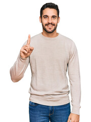 Wall Mural - Young hispanic man wearing casual clothes showing and pointing up with finger number one while smiling confident and happy.