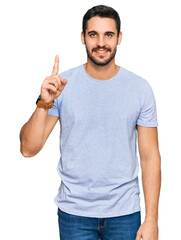 Wall Mural - Young hispanic man wearing casual clothes pointing finger up with successful idea. exited and happy. number one.