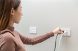 © KMPZZZ - Asian young woman plugged in, unplugged electricity cord cable, put on or remove electric plug cable in socket on wall home outlet for saving, control power electrical energy, eco environment concept.