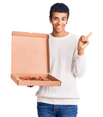 Canvas Print - Young african amercian man holding delivery pizza box smiling happy pointing with hand and finger to the side