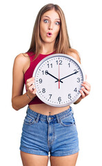 Wall Mural - Young beautiful blonde woman holding big clock scared and amazed with open mouth for surprise, disbelief face