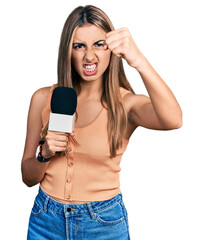 Sticker - Hispanic young woman holding reporter microphone annoyed and frustrated shouting with anger, yelling crazy with anger and hand raised