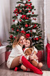 Pretty little girl with a Christmas toy deer and a young smiling mom against the background of the Christmas tree (New Year, 2024, Christmas - concept)
