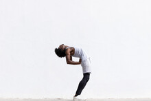 Black Athlete Stretching Body Over White Wall