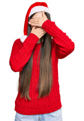 Wall Mural - Young chinese woman wearing christmas hat covering eyes and mouth with hands, surprised and shocked. hiding emotion