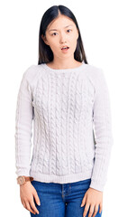 Sticker - Young beautiful chinese woman wearing casual sweater in shock face, looking skeptical and sarcastic, surprised with open mouth