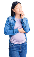 Poster - Young beautiful chinese woman pregnant expecting baby with hand on chin thinking about question, pensive expression. smiling and thoughtful face. doubt concept.