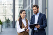 © Liubomir - A young business man and a business woman stand outside the office center and discuss the documents they are holding in their hands.