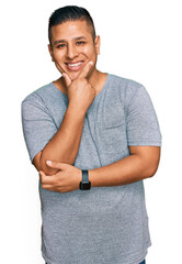 Canvas Print - Young latin man wearing casual clothes looking confident at the camera smiling with crossed arms and hand raised on chin. thinking positive.