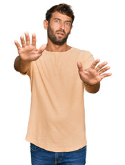 Sticker - Handsome young man with beard wearing casual tshirt doing stop gesture with hands palms, angry and frustration expression