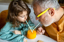 Senior Man And Girl Drinking Fruit Juice On Table