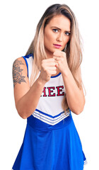 Wall Mural - Young beautiful blonde woman wearing cheerleader uniform ready to fight with fist defense gesture, angry and upset face, afraid of problem