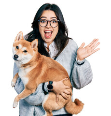 Wall Mural - Beautiful hispanic woman holding cute dog celebrating crazy and amazed for success with open eyes screaming excited.