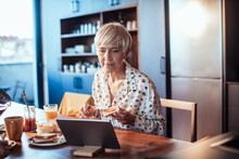 Mature senior woman eating breakfast with tablet at table