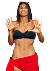 Wall Mural - Young african american woman wearing bikini afraid and terrified with fear expression stop gesture with hands, shouting in shock. panic concept.