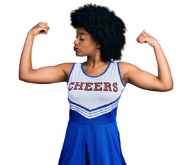 Canvas Print - Young african american woman wearing cheerleader uniform showing arms muscles smiling proud. fitness concept.