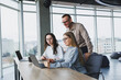 © DSMT - Three employees in a modern office, a man and a woman work at a table, colleagues discuss and consult, thinking about a joint project.