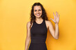 Sporty woman in active wear, yellow backdrop, smiling cheerful showing number five with fingers.