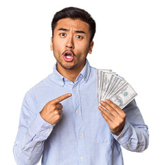 Young Chinese man holding dollar bills in studio pointing to the side