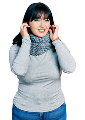 Canvas Print - Young hispanic plus size woman wearing winter scarf covering ears with fingers with annoyed expression for the noise of loud music. deaf concept.