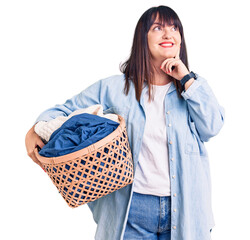 Wall Mural - Young plus size woman holding laundry basket serious face thinking about question with hand on chin, thoughtful about confusing idea