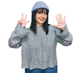 Wall Mural - Young hispanic woman wearing cute wool cap showing and pointing up with fingers number eight while smiling confident and happy.